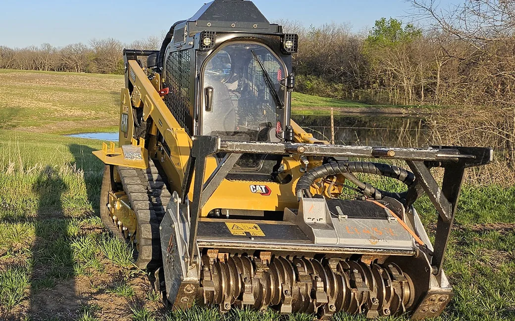 Tracked skid loader with a mulching head in a pasture beside a farm pond, pond construction