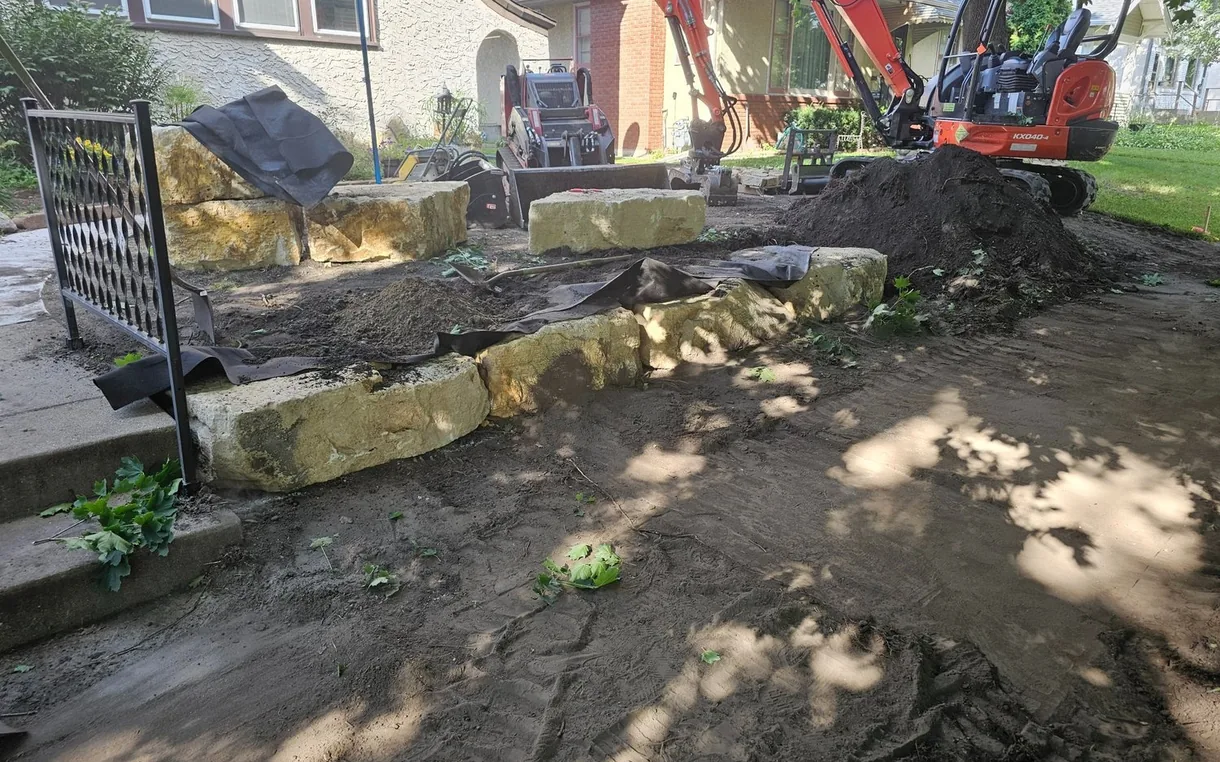 Limestone block retaining wall going in across a front yard with a mini excavator, retaining walls